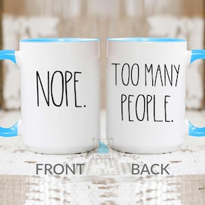 May include: Two white ceramic mugs with blue handles and interiors. One mug reads "NOPE." in black text, and the other reads "TOO MANY PEOPLE." The word "FRONT" is below the first mug, and "BACK" is below the second.