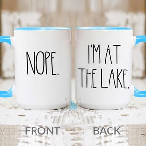May include: White ceramic coffee mug with a blue rim. The front of the mug says "NOPE." The back of the mug says "I'M AT THE LAKE."