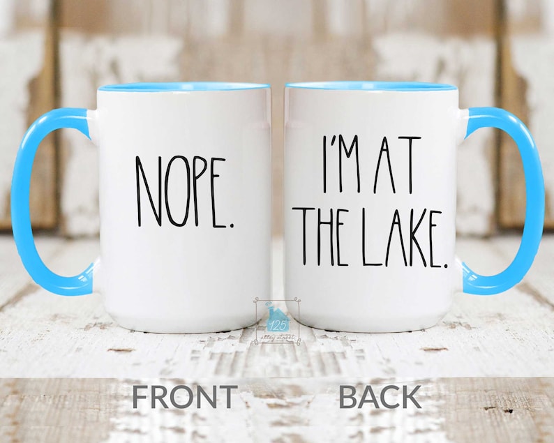 May include: White ceramic coffee mug with a blue rim. The front of the mug says "NOPE." The back of the mug says "I'M AT THE LAKE."