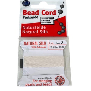 May include: A spool of white natural silk bead cord, 2 metres long, with a needle attached. The cord is 0.50 mm in diameter and is labelled "Natural Silk 100% Naturseide" and "For stringing pearls and beads".