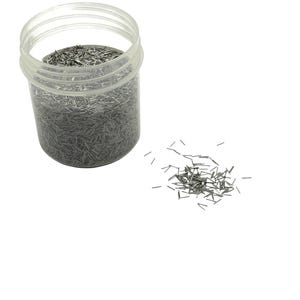 May include: A transparent plastic jar containing numerous small, silver metal pins. A small pile of pins is scattered beside the jar on a white backdrop. The pins are straight and of a consistent length.