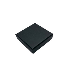 May include: A black square box with a smooth, matt finish. The box is closed and appears to be made of sturdy cardboard.