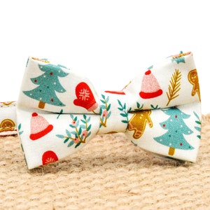 May include: A white Christmas-themed bow tie with a red, green and gold pattern. The bow tie is attached to a red and white collar with a gold bell.