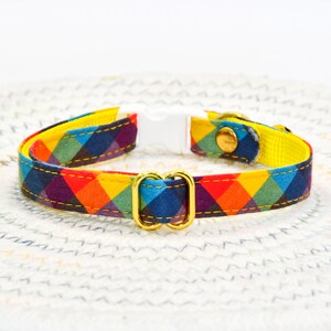 May include: A colorful plaid cat collar with a yellow base and gold metal buckle. The collar has a white plastic safety release buckle.