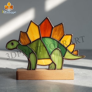 Op de afbeelding: Een gebrandschilderde Stegosaurus-figuur op een houten voet. De dinosaurus heeft een groen lichaam, gele en oranje platen en een bruine omtrek. Het beeldje is een decoratief item.