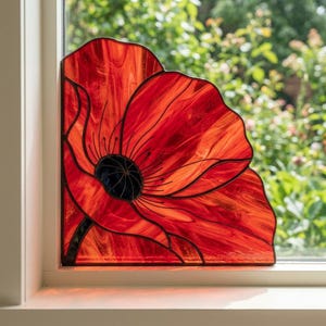May include: A stained glass suncatcher shaped like a quarter of a poppy flower, featuring vibrant red marbled glass petals with dark black glass center details and thin black metal lead lines, positioned against a window pane.