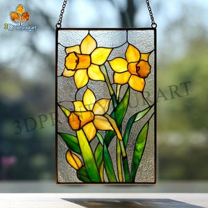 Puede incluir: Panel de vidrieras con narcisos amarillos con centros naranjas y hojas verdes. La obra de arte está enmarcada en metal oscuro y cuelga de una cadena. El panel tiene un fondo de vidrio texturizado.