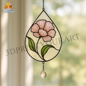 Peut inclure: Un capteur de soleil en vitrail en forme de goutte d'eau, représentant une fleur rose avec des feuilles vertes. Le capteur de soleil a un fond clair et texturé et un petit pendentif en cristal. Le design est encadré de métal noir.