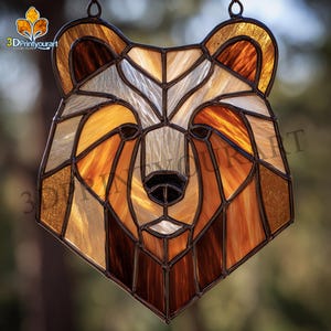 Puede incluir: Cabeza de oso de vidriera con diseño geométrico. La obra presenta tonos marrones, ámbar y crema, con nariz negra y contornos marrón oscuro. La pieza está diseñada para colgar, mostrando un tema inspirado en la naturaleza.