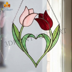 May include: Stained glass tulip art piece with a heart-shaped design. The piece features two tulips, one pink and one red, with green leaves and stems. The artwork is suspended by a chain and is suitable for window display.