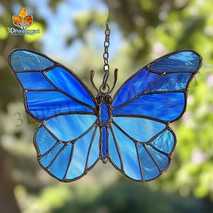 May include: A stained glass butterfly suncatcher with a blue and white color scheme. The butterfly is hanging from a silver chain.