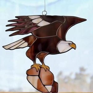 May include: A stained glass bald eagle with brown and white feathers, perched on a brown rock. The eagle is in flight with its wings spread out.