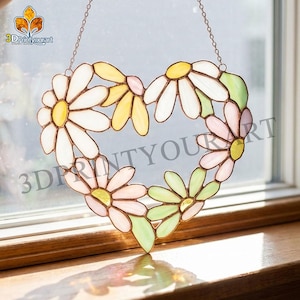 May include: Stained glass heart-shaped suncatcher featuring daisy flowers in white, yellow, pink, and green. The suncatcher is suspended by a chain and is displayed in front of a window. The text "3DPrintYourArt" is visible.
