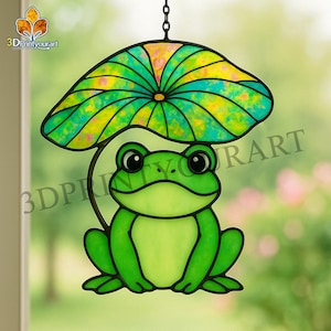 May include: A stained glass frog with a green body and yellow eyes sits under a green and yellow stained glass lily pad. The lily pad is suspended from a black metal chain.