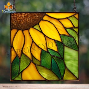 Puede incluir: Panel cuadrado de vidriera con un diseño de girasol. La obra de arte presenta pétalos amarillos, hojas verdes y un centro marrón, todo delineado con líneas oscuras. El panel está suspendido por una cadena e incluye el texto "3DPrintyourart".