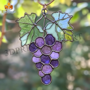 Könnte beinhalten: Ein Buntglas-Sonnenfänger mit einem Weinstock mit grünen Blättern und einer Traube aus violetten Trauben. Der Sonnenfänger hängt an einem Metallring.