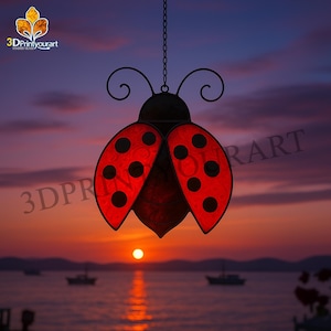 May include: A red and black ladybug-shaped stained glass suncatcher hangs from a chain against a sunset sky. The suncatcher is suspended over a body of water with boats in the distance.