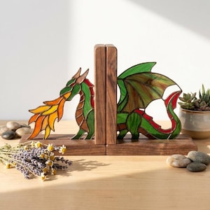 May include: A pair of wooden bookends featuring stained glass dragon panels. One panel shows a green dragon breathing orange and yellow flames, while the other shows the dragon's body and wings in green and red tones, set on a dark wood base.