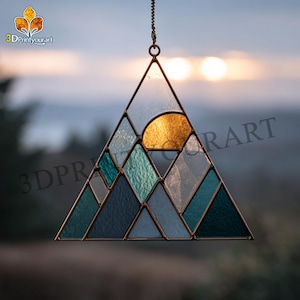 Peut inclure: Une scène de montagne en vitrail avec un soleil doré et diverses nuances de bleu et de vert. L'œuvre d'art est encadrée de métal foncé et suspendue à une chaîne. Le texte "3DPrintyourart" est visible en haut à gauche.