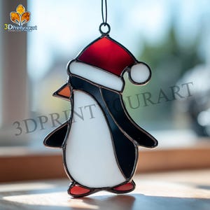 Può includere: Ornamento a forma di pinguino in vetro colorato con cappello di Babbo Natale rosso con bordo bianco. Il pinguino ha corpo nero, pancia bianca, becco arancione e piedi rossi. Il testo "3DPrintyourart" è visibile.