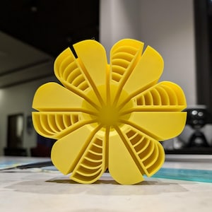 May include: A yellow 3D printed flower with eight petals. Each petal has a series of concentric circles.