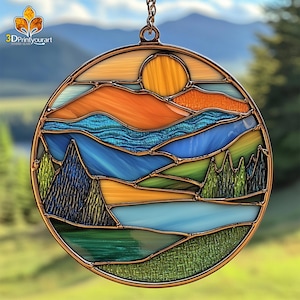 May include: A stained glass suncatcher depicting a mountain landscape with a blue lake, green trees, and an orange sunset. The suncatcher is round and has a copper frame.