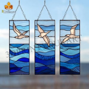 May include: Three rectangular stained glass panels depicting seagulls in flight over a blue ocean. The panels are framed in black and suspended by chains. The ocean is represented by layered blue glass.