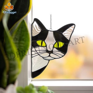 Op de afbeelding: Zwart-witte glas-in-lood kat die om een hoek kijkt. De kat heeft gele ogen en een witte vlek op zijn borst.
