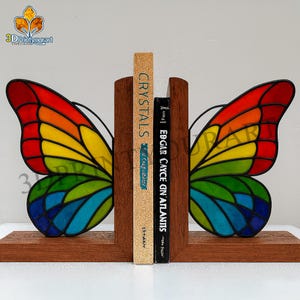 Könnte beinhalten: Schmetterlingsförmige Buchstützen mit bunten Glasflügeln. Die Holz-Buchstützen halten zwei Bücher, eines mit dem Titel "Crystals" und das andere mit dem Titel "Edgar Cayce on Atlantis".