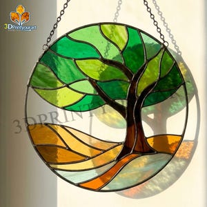 Könnte beinhalten: Rundes Buntglas-Kunstwerk mit einem Baum mit grünen Blättern und einem braunen Stamm. Das Design beinhaltet eine gelbe und orangefarbene Landschaft am unteren Rand. Das Stück wird von einer Kette gehalten und eignet sich für die Heimdekoration.