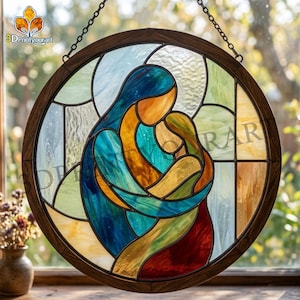 Puede incluir: Vidriera redonda que representa a una madre y un niño en tonos azules, naranjas y amarillos. La obra de arte está enmarcada en un marco de madera marrón oscuro y cuelga de una cadena. La imagen tiene el texto "3DPrintyourart".