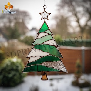 May include: Stained glass Christmas tree ornament with a star topper. The tree features shades of green and white glass, with a bronze-colored metal frame and base. The ornament hangs from a chain. The logo "3DPrintyourart" is visible in the background.