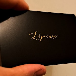 May include: A black card with gold lettering that reads 'L'epicure'