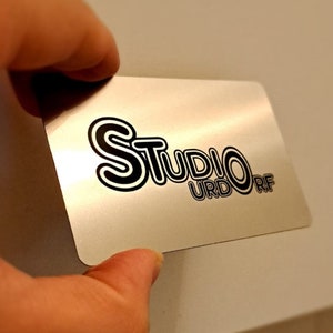 May include: A silver metal business card with black text that reads 'Studio URDORF'.