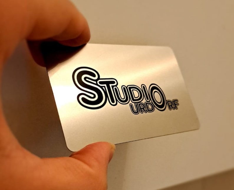 May include: A silver metal business card with black text that reads 'Studio URDORF'.