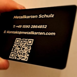 May include: A black metal business card with white text. The text reads 'Metallkarten Schulz', 'T: +49 1590 2864852', 'E Kontakt@metallkarten.com', and a QR code.