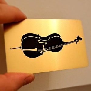 May include: A black silhouette of a cello on a gold background.
