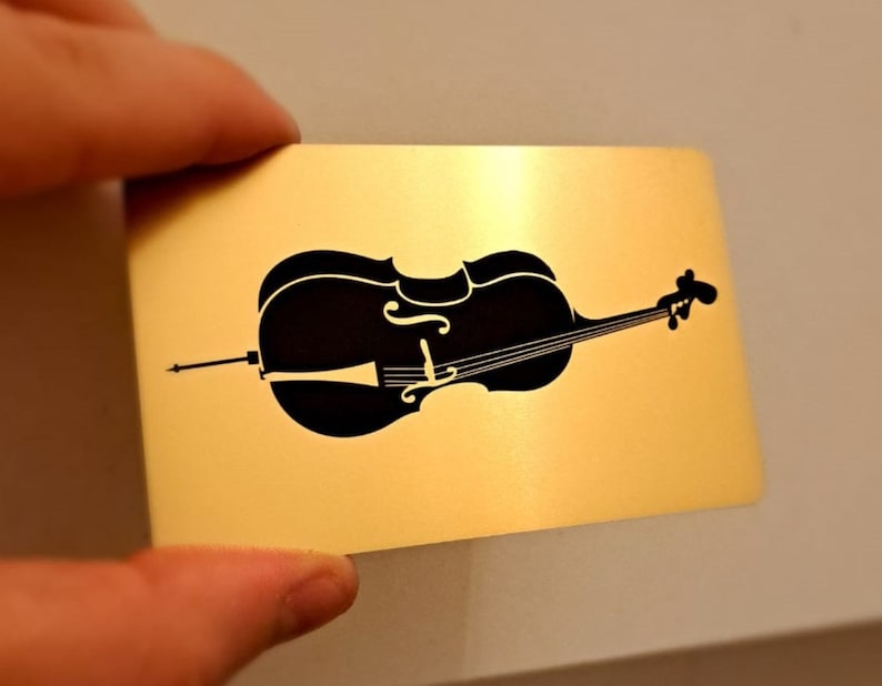 May include: A black silhouette of a cello on a gold background.