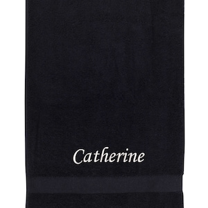 May include: A black bath towel with the name "Catherine" embroidered in white on the front.