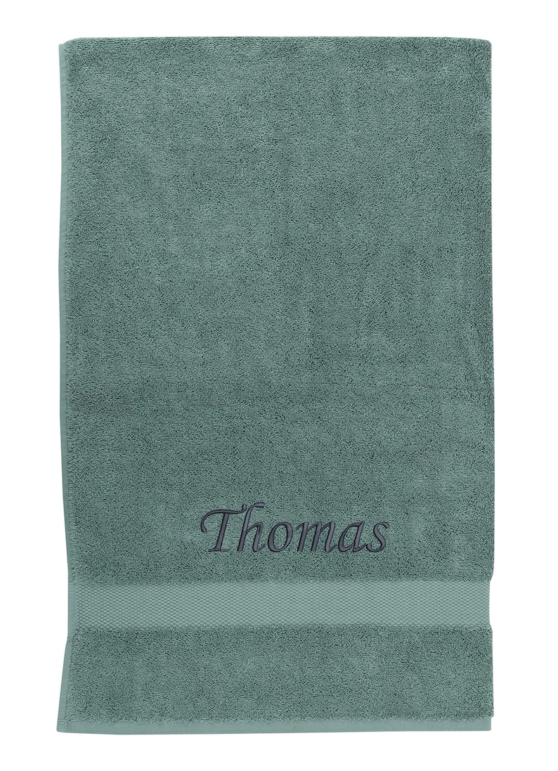 May include: A teal bath towel with the name "Thomas" embroidered in black thread.