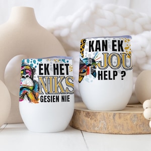 Könnte beinhalten: Zwei weiße Weingläser ohne Stiel mit Deckel. Eines zeigt eine farbenfrohe Affengrafik und den Text "EK HET NIKS GESIEN NIE". Das andere hat ein Muster und den Text "KAN EK JOU HELP?"
