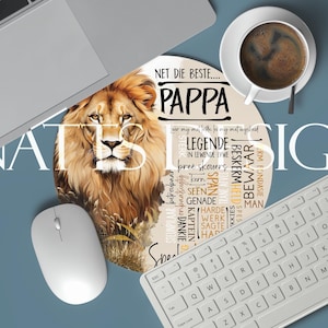 May include: Round mousepad featuring a majestic lion with a golden mane. The mousepad has the word "PAPPA" and other text in a circular design. A cup of coffee, a keyboard, and a mouse are also visible.