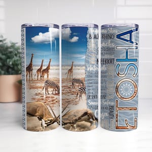 May include: A cylindrical tumbler featuring a wrap-around African savanna scene with giraffes, zebras, and an oryx. The design includes the text ETOSHA in large letters, along with words like Salt Pan, Dust Trails, and Safari against a blue sky.