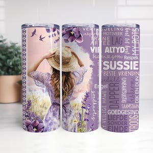 Może przedstawiać: Kubek ze stali nierdzewnej z owiniętym wzorem przedstawiającym kobietę w lawendowej sukience i słomkowym kapeluszu na polu lawendy. Kubek ma fioletową kwiatową obwódkę i tekst.