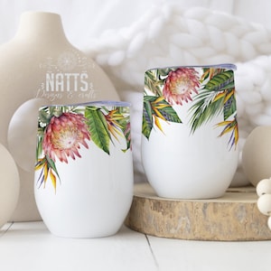 May include: Two white stainless steel tumblers with a tropical floral design featuring pink proteas and green leaves. The tumblers are on a wooden surface with a white vase and a string of wooden beads.