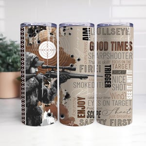 Puede incluir: Un juego de tres vasos aislados de acero inoxidable. Cada vaso presenta un diseño con un tirador apuntando con un rifle, un objetivo y texto como "BullsEye", "Good Times" y "Safety First". La combinación de colores incluye marrón, beige y negro.