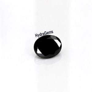 Peut inclure: Une pierre précieuse noire de forme ovale et facettée. La gemme est très réfléchissante, avec des reflets blancs brillants. Le texte "HydraGems" est imprimé en noir au-dessus de la gemme.