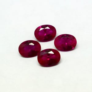 Peut inclure: Quatre rubis ovales et facettés sont présentés sur un fond blanc. Les pierres précieuses sont d'un rouge profond et vibrant, avec de multiples facettes captant la lumière. Les rubis sont disposés en carré légèrement décalé.
