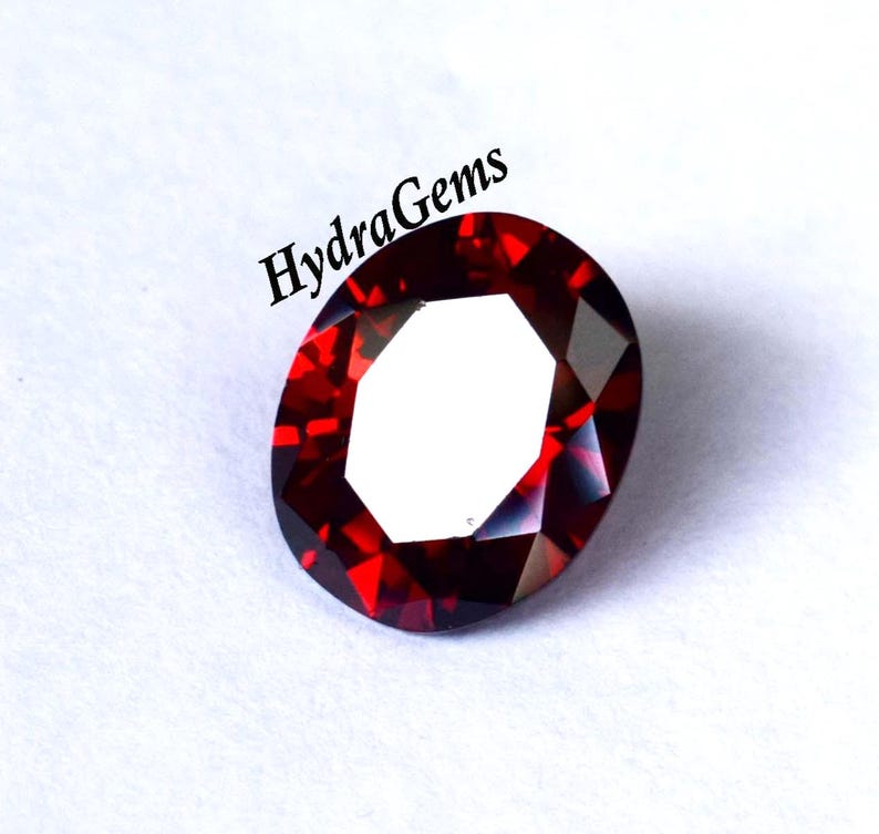 K&ouml;nnte beinhalten: Ein facettierter, oval geformter, tiefroter Edelstein. Der Edelstein hat eine helle, reflektierende Oberfl&auml;che mit einem wei&szlig;en Zentrum. Der Text "HydraGems" ist in Schwarz oben links im Bild gedruckt. Der Edelstein ist vor wei&szlig;em Hintergrund.