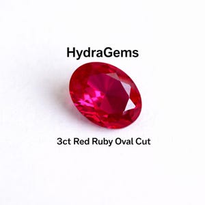 May include: A vibrant red, oval-cut ruby gemstone. The gem is 3ct and features a polished surface. The image includes the text "HydraGems" and "3ct Red Ruby Oval Cut".